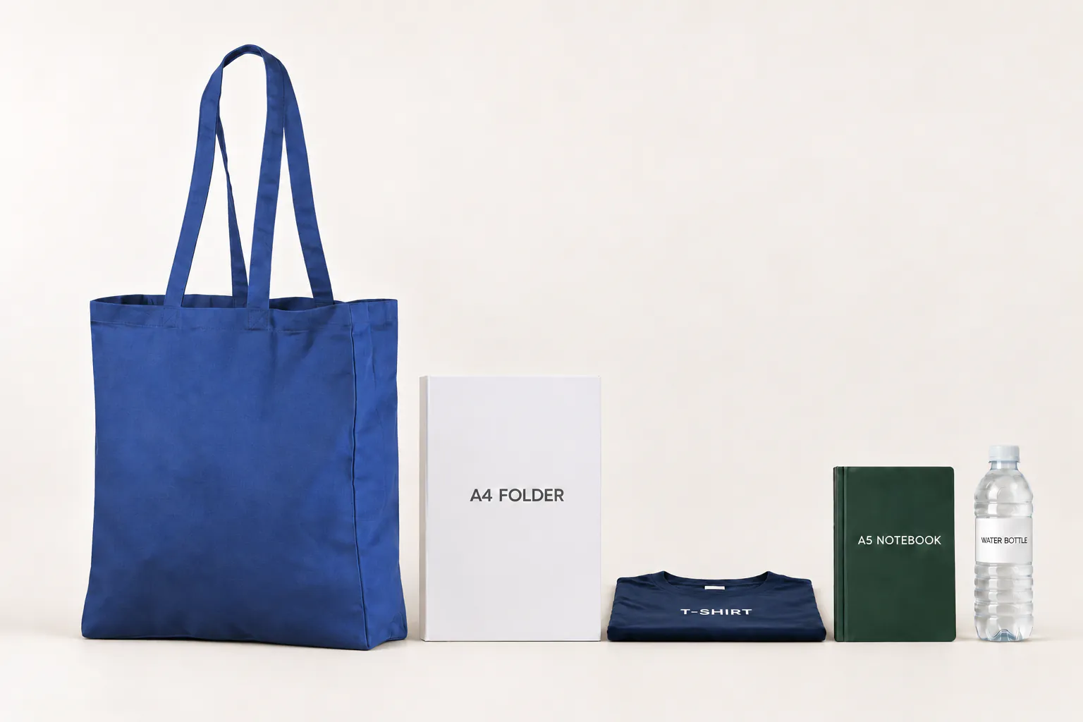 Kongeblå bomuldspose med fals ved siden af en A4-mappe, en foldet T-shirt, en A5-notesbog og en drikkeflaske.